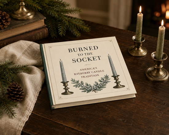 Book titled 'Burned to the Socket' on a wooden surface with candles and greenery.
